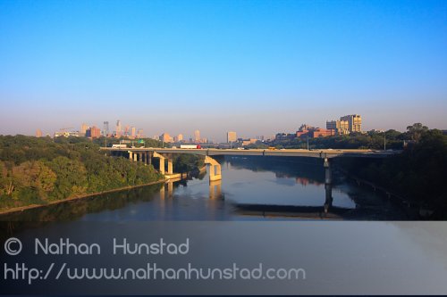 Downtown Minneapolis and the University of Minnesota campus during rush hour from the Franklin Avenue Bridge. The Interstate 94 bridge across the river can be seen.